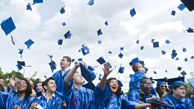 Absolventinnen und Absolventen des Queensbury Union Free School District werfen ihre Hüte bei der Abschlussfeier in die Luft vor bewölktem Himmel.