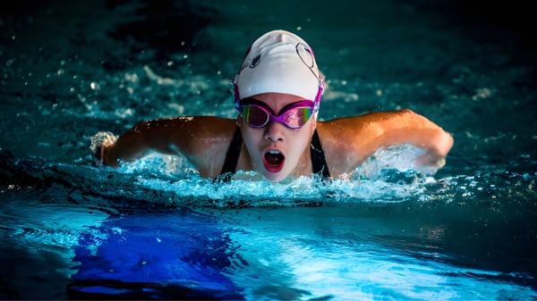 Eine Schwimmerin mit Schwimmbrille und roter Badekappe beim kraftvollen Schwimmen auf dem Campus der Queenswood School.