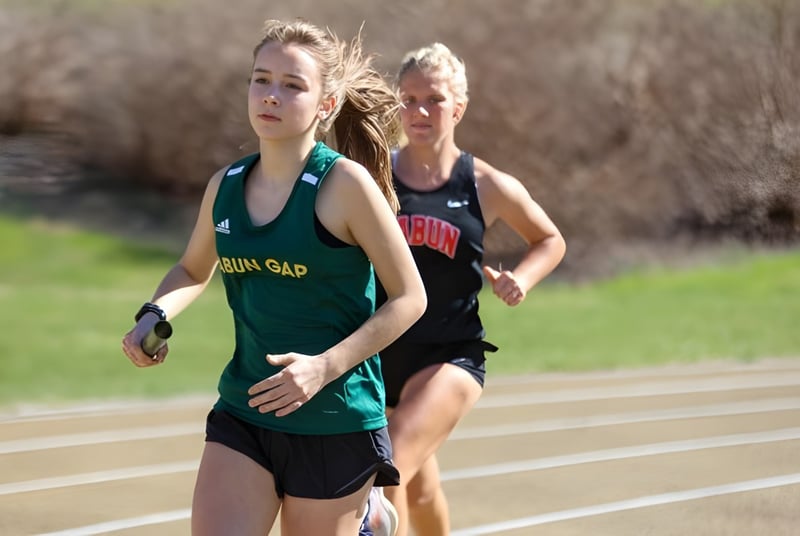 Zwei weibliche Athletinnen laufen auf der Laufbahn der Rabun Gap-Nacoochee School, eine trägt ein grünes Trikot, die andere ein schwarzes.