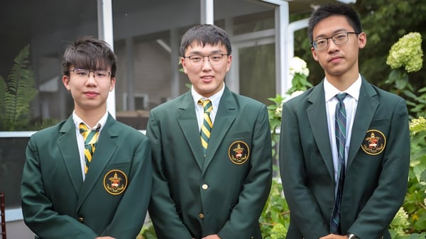 Drei Schüler der Rabun Gap-Nacoochee School stehen vor einem Gebäude mit Garten im Hintergrund.