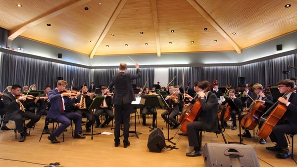 Das Orchester des Radley College führt ein Konzert unter der Leitung des Dirigenten auf der Bühne mit gewölbter Holzdecke auf.