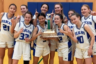 Eine Gruppe junger Basketballspielerinnen der École Secondaire R.A. McMath Secondary School feiert ihren Sieg mit einem Pokal auf dem Basketballfeld.