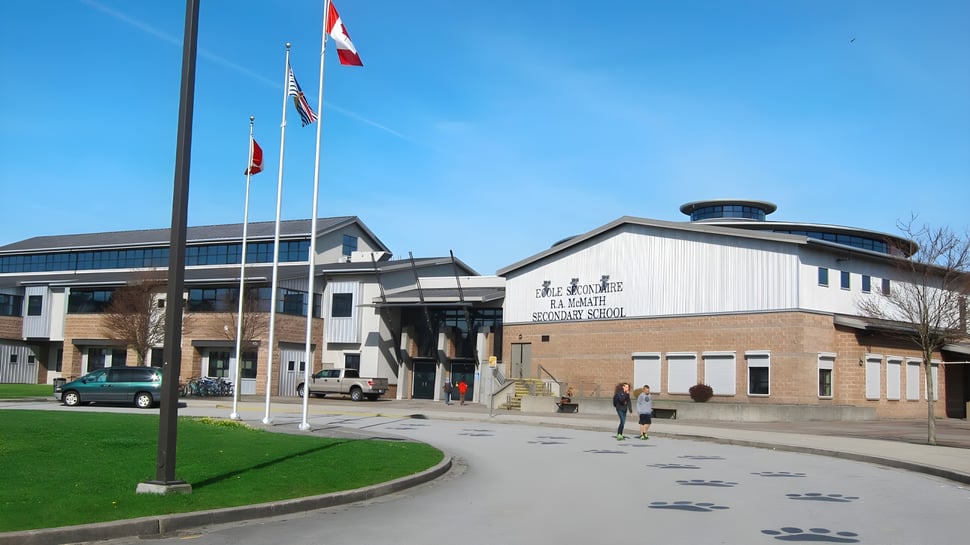 Das moderne mehrstöckige Gebäude der École Secondaire R.A. McMath Secondary School mit Flaggen und einem Weg im Vordergrund.