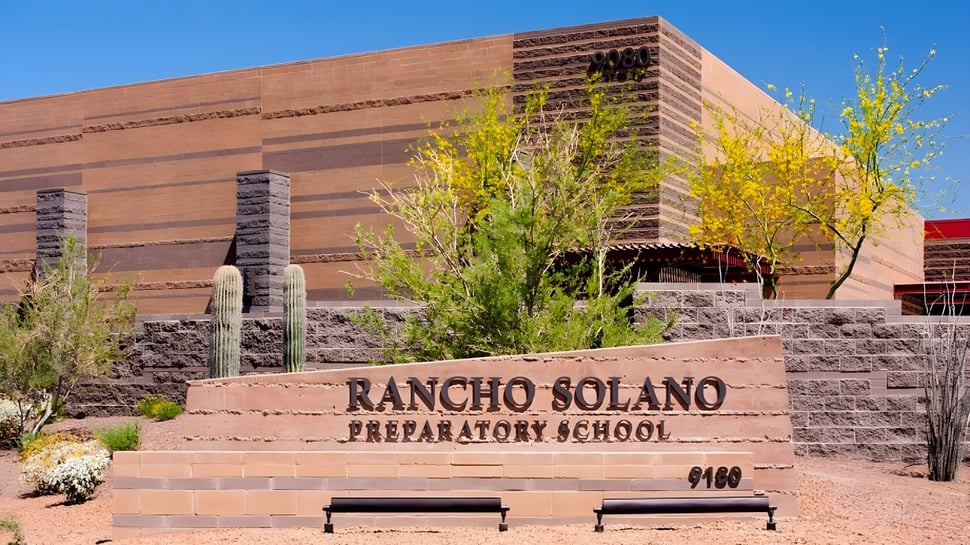 Das Backsteingebäude der Rancho Solano Preparatory School mit Namensschriftzug ist umgeben von Bäumen und einer Steinmauer.