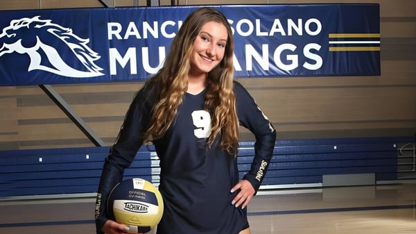 Eine Schülerin der Rancho Solano Preparatory School steht vor einem Banner der Mustangs und hält einen Volleyball.