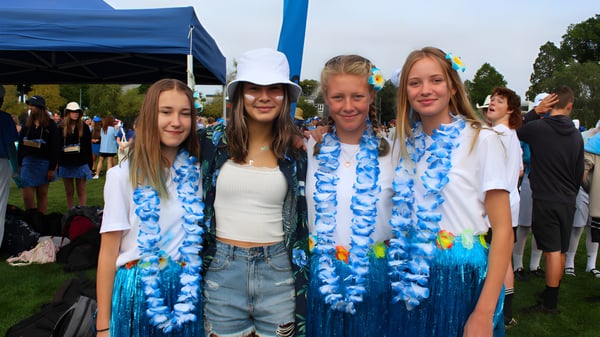 Eine Gruppe von Schülerinnen der Rangiora High School trägt bunte Blumenketten vor einem blauen Zelt bei einer Outdoor-Veranstaltung.