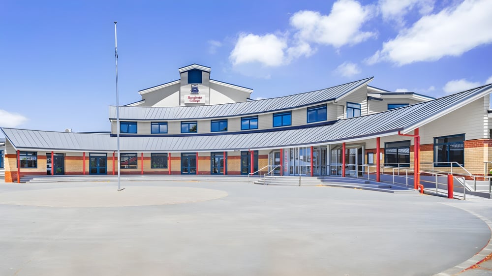 Das moderne mehrstöckige Gebäude mit geschwungenem Dach und großen Fenstern des Rangitoto College ist von einem gepflasterten Außenbereich umgeben.