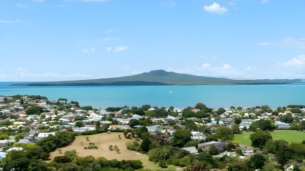 Blick auf die Küstenlandschaft mit einer türkisfarbenen Bucht und Bergen im Hintergrund nahe dem Rangitoto College.