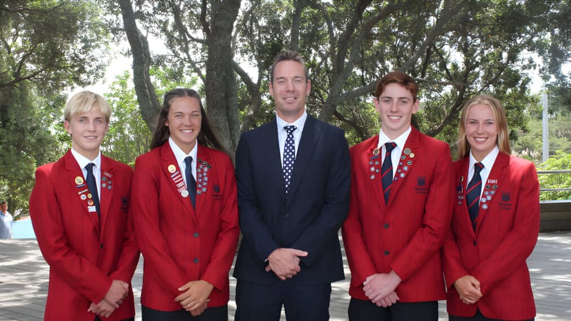Eine Gruppe von fünf Schülern in roten Uniformen steht auf dem Gelände des Rangitoto College im Wald.