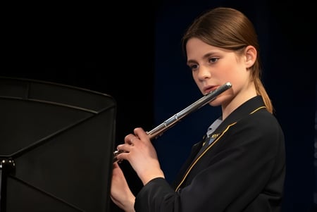 Eine Schülerin des Ratcliffe College spielt eine Flöte auf der Bühne vor schwarzem Hintergrund.