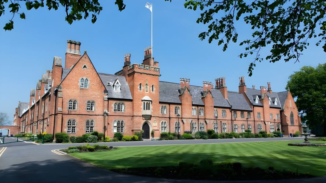 Das große Backsteingebäude mit Türmen und Kaminen auf dem Gelände des Ratcliffe College ist von gepflegtem Rasen und Bäumen umgeben.