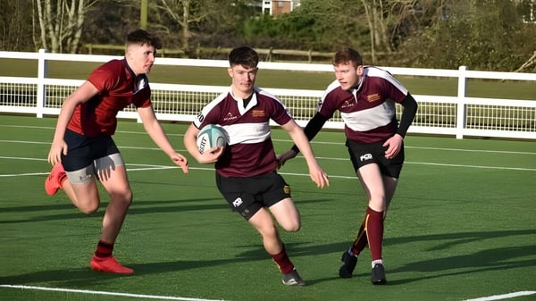Drei Schüler des Ratcliffe College spielen Rugby auf einem grasbewachsenen Spielfeld mit Bäumen und Zaun im Hintergrund.