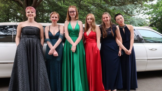 Eine Gruppe junger Frauen der Rathdown School steht in formellen Abendkleidern vor einem geparkten Fahrzeug im Freien.