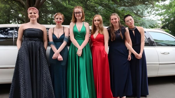 Eine Gruppe junger Frauen der Rathdown School posiert vor einer weißen Limousine in einem bewaldeten Bereich.