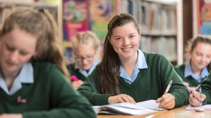 Schüler der Rathdown School sitzen im Klassenzimmer an Tischen umgeben von Bücherregalen und bunten Bildern an den Wänden.