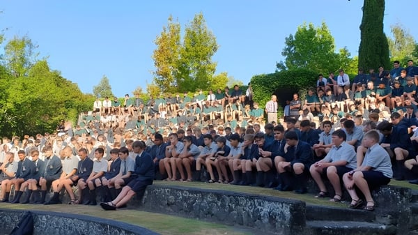 Eine Gruppe von Schülerinnen und Schülern sitzt auf einer Steinmauer vor Bäumen auf dem Gelände des Rathkeale College.