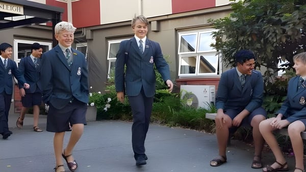 Eine Gruppe von Schülerinnen und Schülern in Schuluniform steht vor einem Gebäude mit Garten auf dem Campus von Rathkeale College.