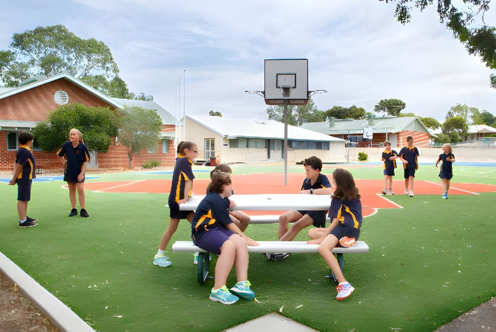 Eine Gruppe Schüler spielt Basketball auf dem Sportplatz der Ravensthorpe District High School, umgeben von Backsteingebäuden und Bäumen.