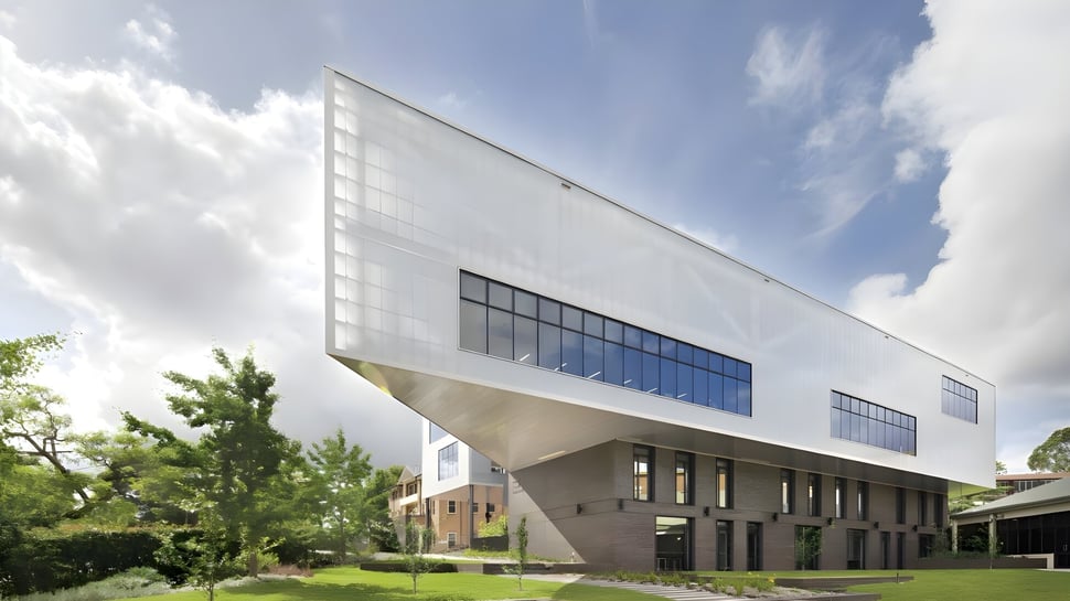 Das moderne Gebäude der Ravenswood School for Girls mit großen Fenstern und umgeben von grüner Landschaft ist vor bewölktem Himmel zu sehen.
