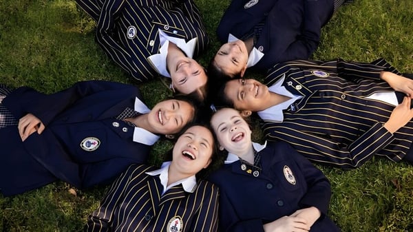 Eine Gruppe Schülerinnen der Ravenswood School for Girls liegt lachend auf dem Gras im Freien.