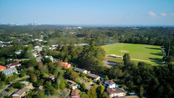 Ein weitläufiges grünes Feld mit Wald und Wohnhäusern im Hintergrund nahe der Ravenswood School for Girls.