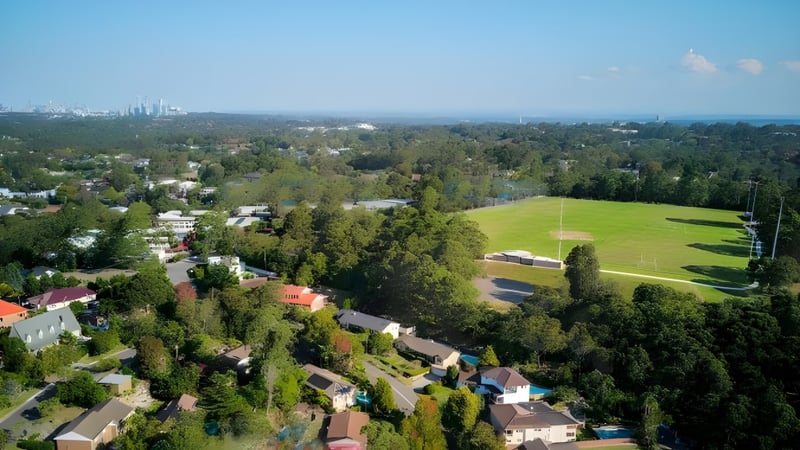 Ein weitläufiges grünes Feld mit Wald und Wohnhäusern im Hintergrund nahe der Ravenswood School for Girls.