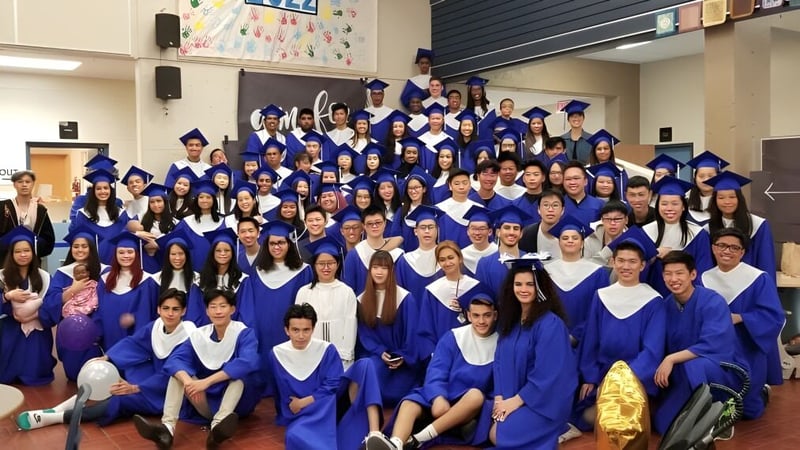 Eine große Gruppe von Absolventinnen und Absolventen der R.C. Palmer Secondary School posiert in blauen Talaren in einem Klassenzimmer.