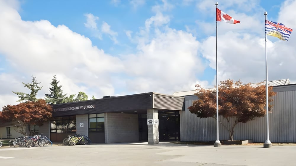 Das moderne schwarze Gebäude der R.C. Palmer Secondary School ist von Bäumen umgeben und zeigt verschiedene Länderflaggen im Außenbereich.