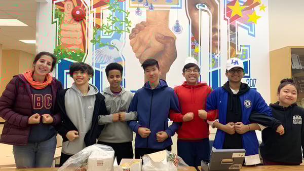 Eine Gruppe von Schülerinnen und Schülern steht vor einem farbenfrohen Wandgemälde auf dem Campus der R.C. Palmer Secondary School.