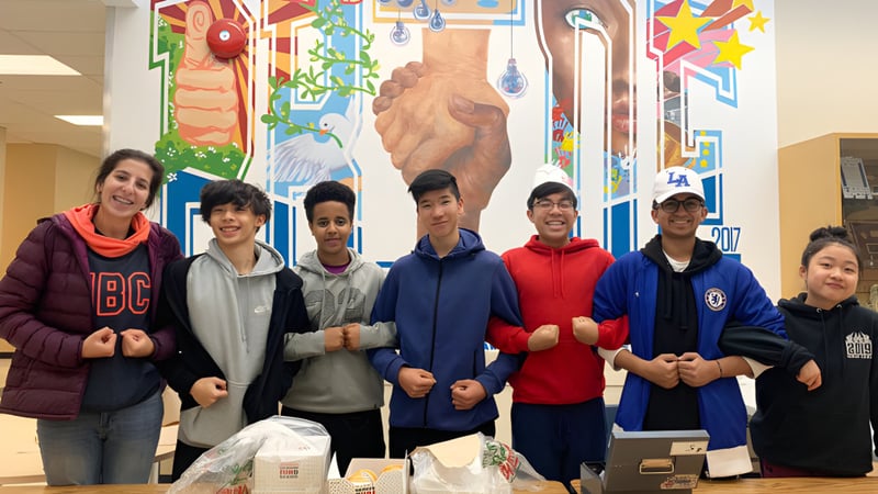 Eine Gruppe von Schülerinnen und Schülern steht vor einem farbenfrohen Wandgemälde auf dem Campus der R.C. Palmer Secondary School.