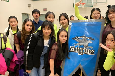 Eine Gruppe Schülerinnen der R.C. Palmer Secondary School posiert mit einem großen blauen Banner mit Sportteam-Logo.