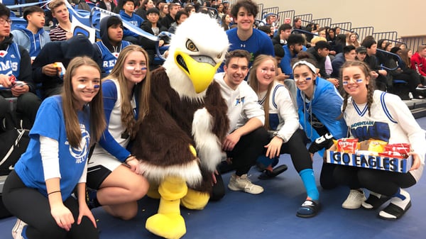 Schülerinnen und Schüler der R.E. Mountain Secondary School posieren mit dem großen Maskottchen bei einer Schulveranstaltung.