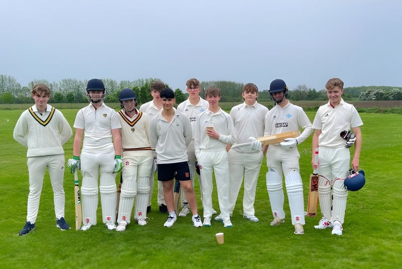 Eine Gruppe junger Cricket-Spieler in weißen Uniformen steht auf dem Spielfeld der Read School vor Bäumen.