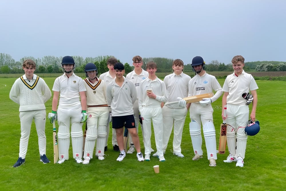 Eine Gruppe junger Cricket-Spieler in weißen Uniformen steht auf dem Spielfeld der Read School vor Bäumen.