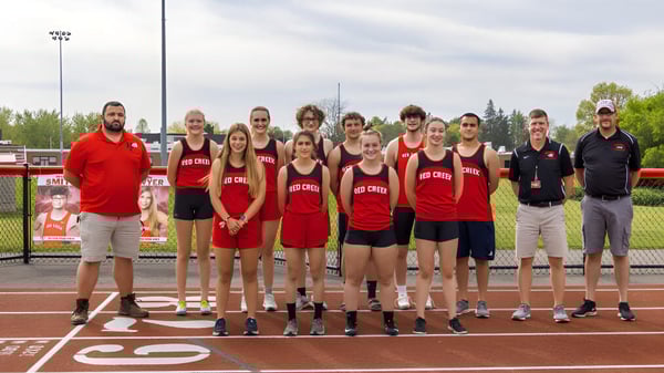 Eine Gruppe von Athleten in roten Uniformen steht auf dem Sportplatz der Red Creek High School unter einem bewölkten Himmel.