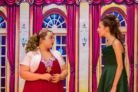 Zwei Schülerinnen der Red Creek High School stehen vor einem farbenfrohen Hintergrund mit Bögen und Vorhängen.