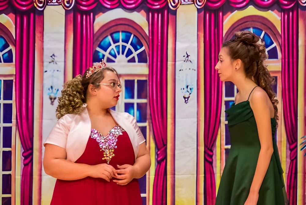 Zwei Schülerinnen der Red Creek High School stehen vor einem farbenfrohen Hintergrund mit Bögen und Vorhängen.