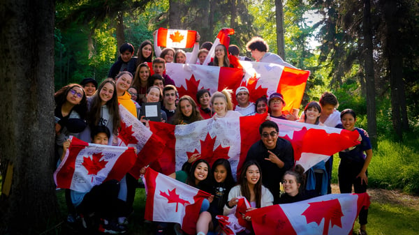 Schülerinnen und Schüler der Red Deer Public Schools feiern im Wald mit kanadischen Flaggen bei einer patriotischen Veranstaltung.