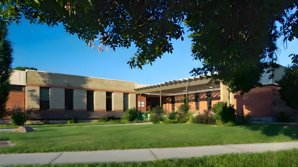 Das moderne Backsteingebäude mit überdachtem Eingang der Red Deer Public Schools ist von gepflegtem Rasen und Bäumen umgeben.