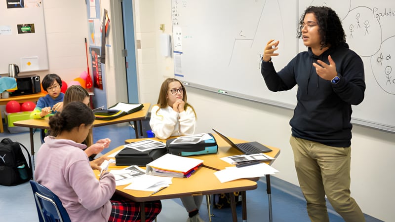 Schüler und eine Lehrkraft von Red Deer Public Schools diskutieren gemeinsam im Klassenraum mit Lernmaterialien und Technologie im Hintergrund.