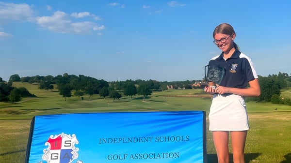 Eine Schülerin der Reddam House Berkshire steht vor einem Schild der Independent Schools Golf Association mit Golfplatz und Wald im Hintergrund.