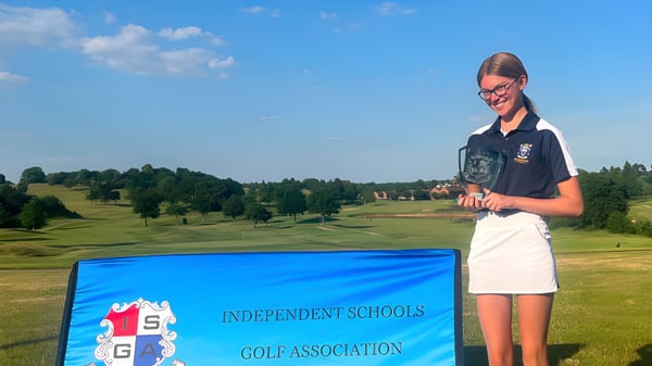 Eine Schülerin der Reddam House Berkshire steht in Schuluniform auf einem Golfplatz mit Bäumen und Hügeln im Hintergrund.