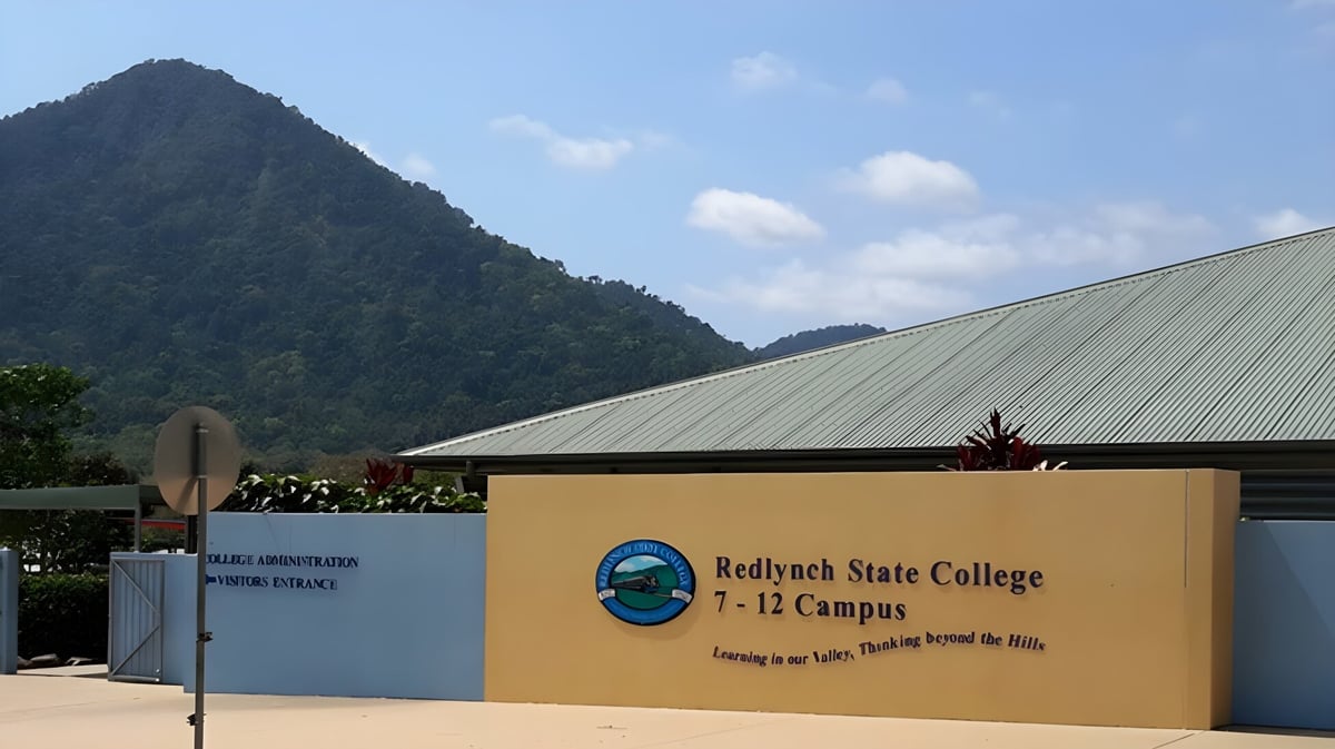 Das gelbe Gebäude mit dem Redlynch State College Logo vor einer bergigen Landschaft.