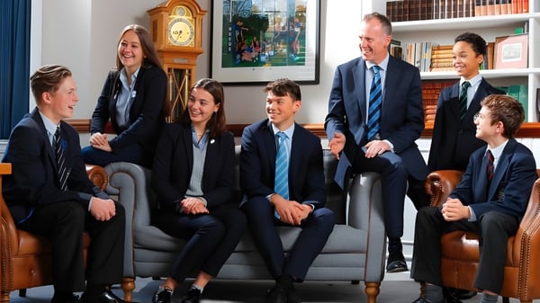 Eine Gruppe von Schülerinnen und Schülern befindet sich in einem Raum mit großer Uhr und Bücherregalen auf dem Campus der Reed’s School.