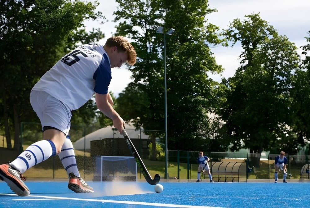 Ein Schüler der Reed’s School spielt Feldhockey auf einem blauen Kunstrasenplatz mit anderen Spielern im Hintergrund.