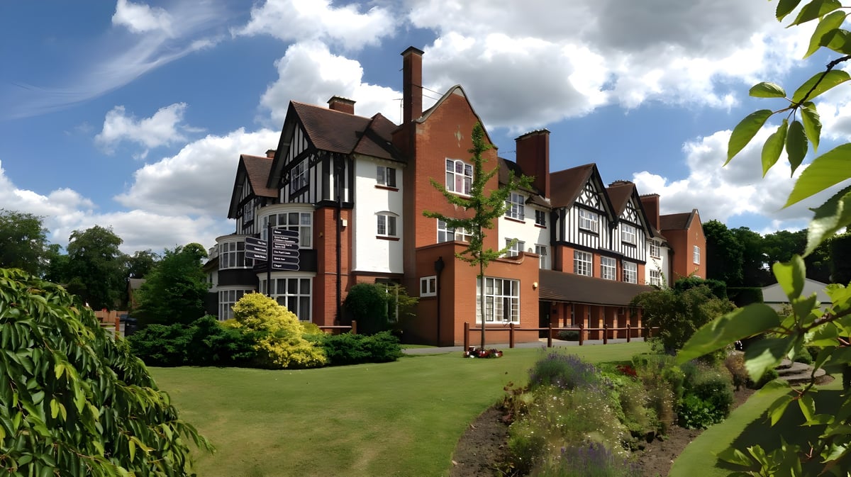 Das Tudor-Gebäude der Reed’s School ist von einem gepflegten Garten mit Rasen und grünem Laub umgeben.