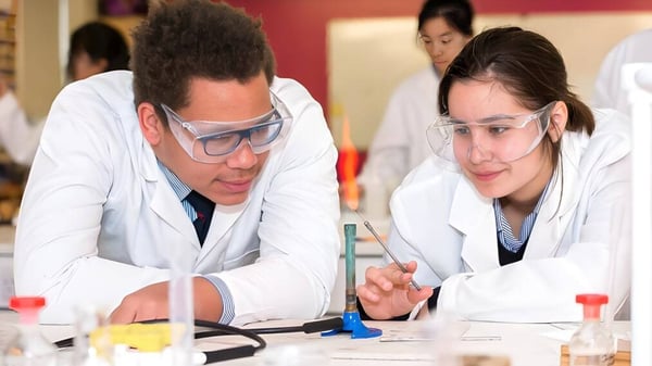 Zwei Schüler des Rendcomb College konzentrieren sich in weißen Laborkitteln auf ein Experiment im Labor.