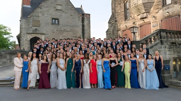 Eine große Gruppe von Schülerinnen im formellen Outfit steht vor dem historischen Stein-Gebäude auf dem Campus der Repton School.