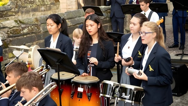 Schüler der Repton School spielen vor einem Steingebäude verschiedene Schlaginstrumente.