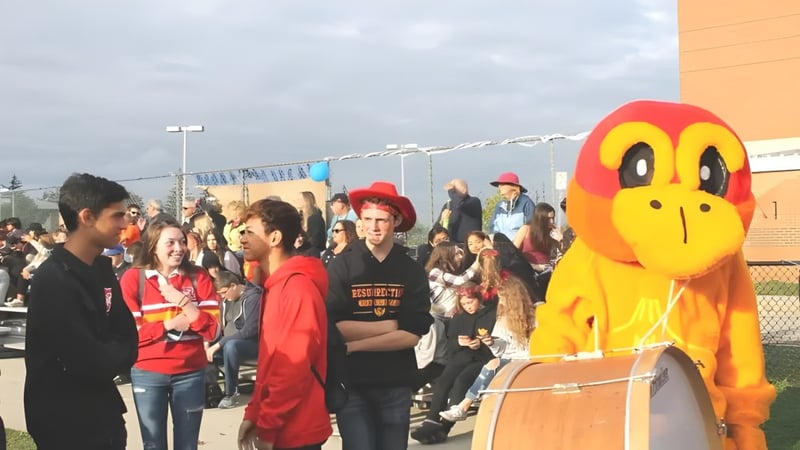 Eine große gelbe Cartoonfigur steht vor einer Menschenmenge auf dem Gelände der Resurrection Catholic School.